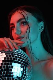 Beautiful woman with disco ball posing in neon lights against black background