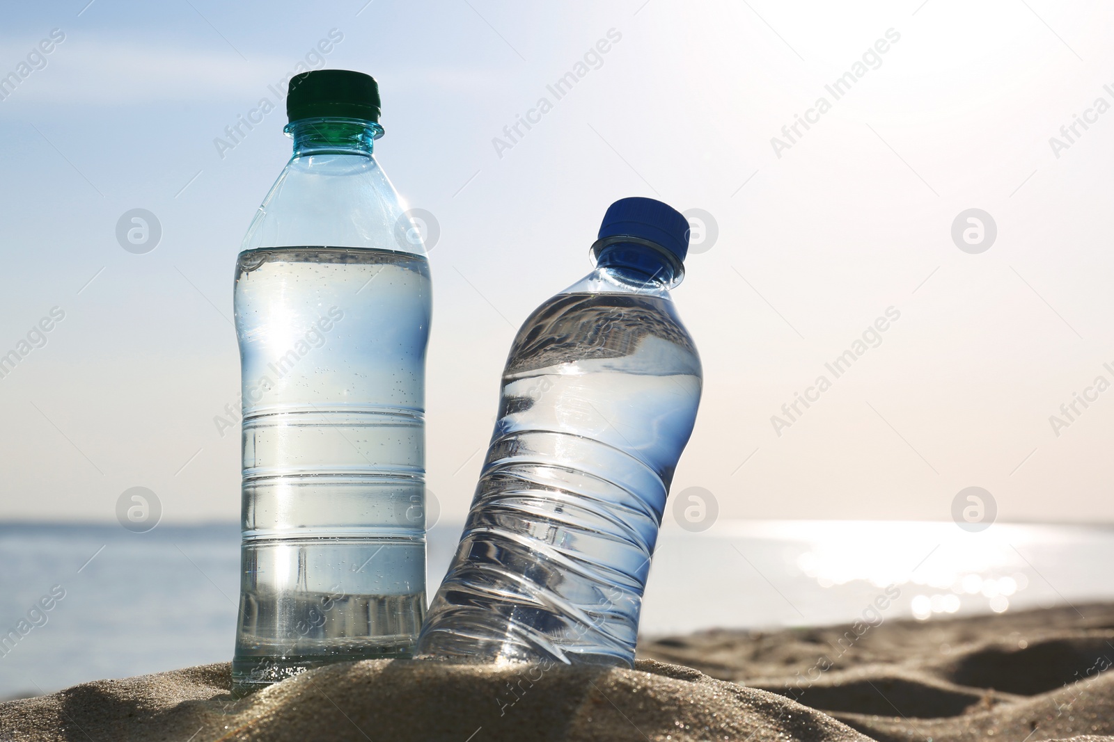 Photo of Sandy beach with bottles of refreshing drink on hot summer day, space for text