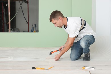 Photo of Man using hammer during installation of new laminate flooring in room
