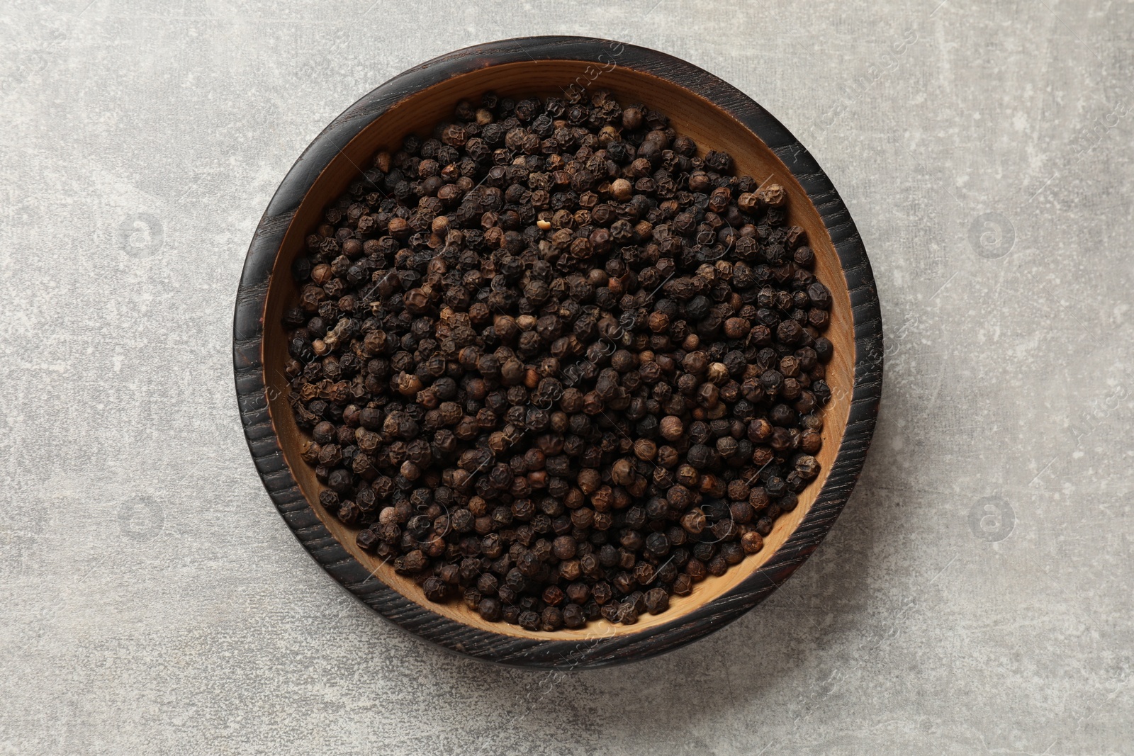 Photo of Aromatic spice. Black pepper in bowl on light grey table, top view