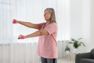 Photo of Senior woman exercising with dumbbells at home. Sports equipment