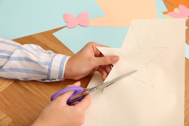 Woman cutting color paper with scissors at wooden table, closeup