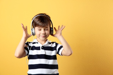 Photo of Cute little boy listening to music with headphones on color background. Space for text