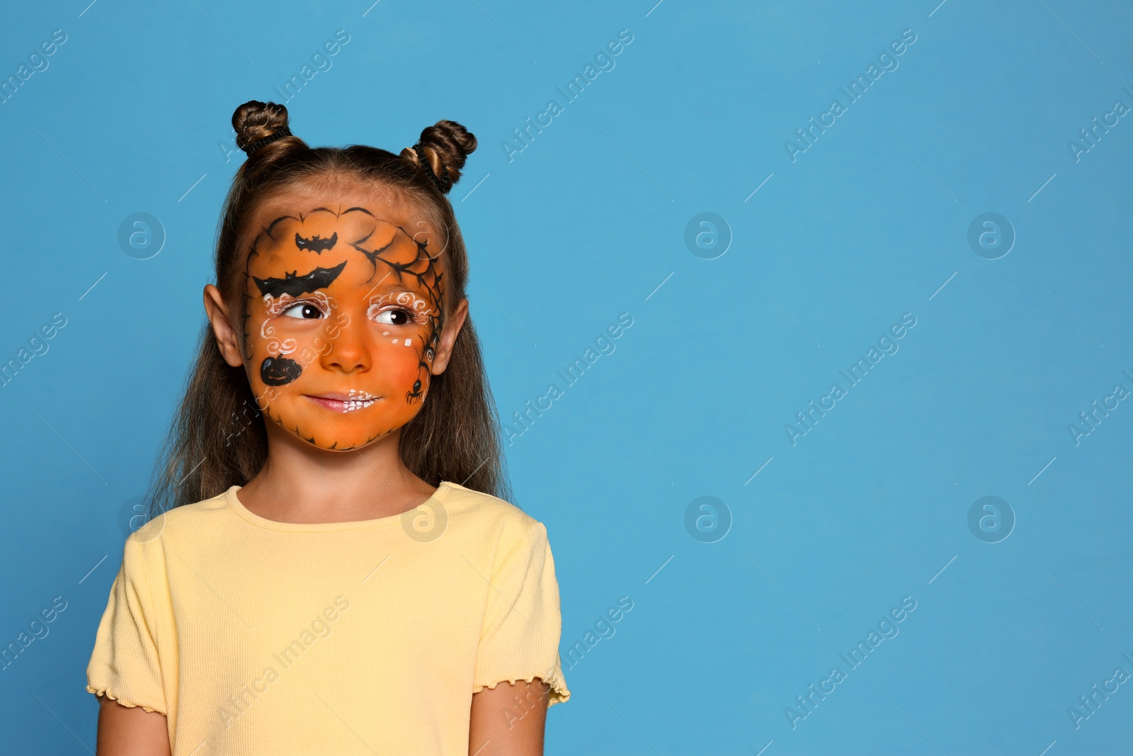 Photo of Cute little girl with face painting on blue background. Space for text