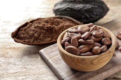 Bowl with cocoa beans on wooden table, space for text