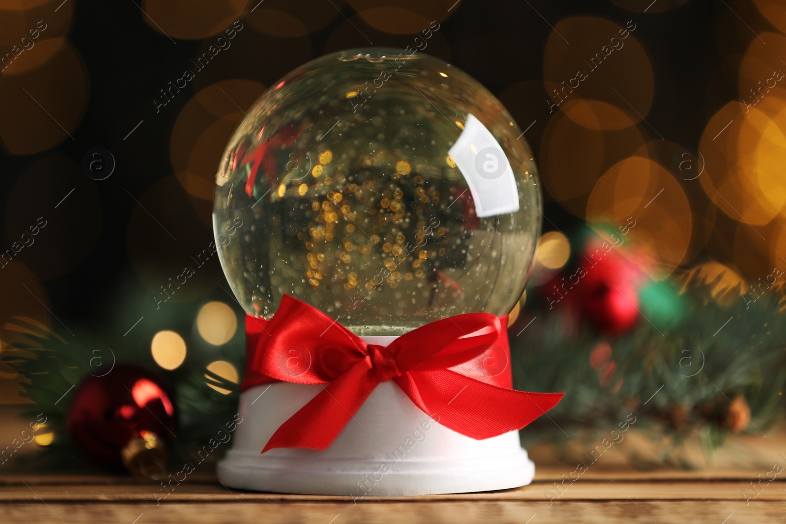 Photo of Beautiful snow globe on wooden table against blurred Christmas lights, closeup