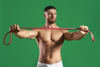 Photo of Muscular man exercising with elastic resistance band on green background