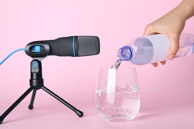 Photo of Woman making ASMR sounds with microphone and water on pink background, closeup