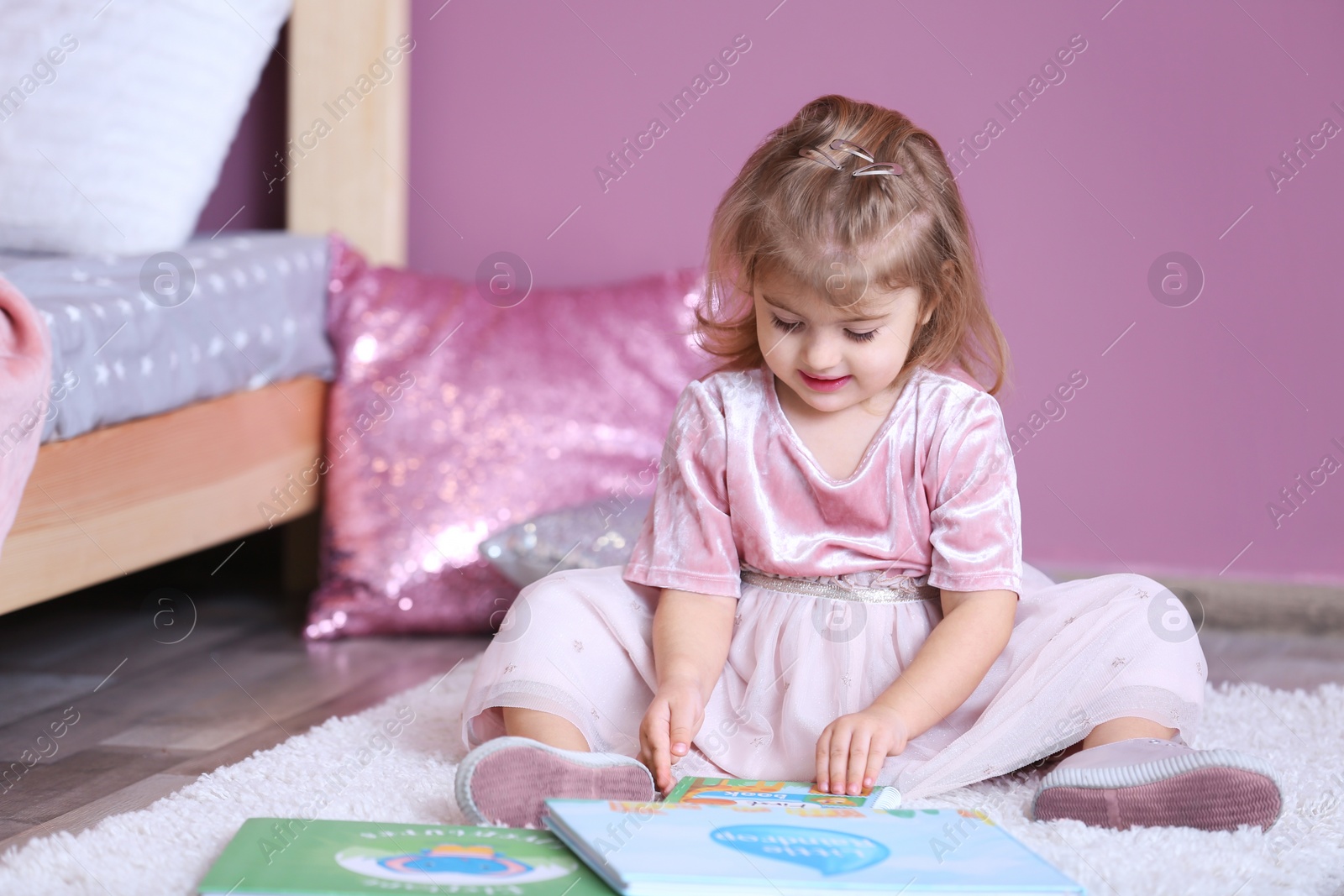 Photo of Cute little girl in princess dress reading book at home