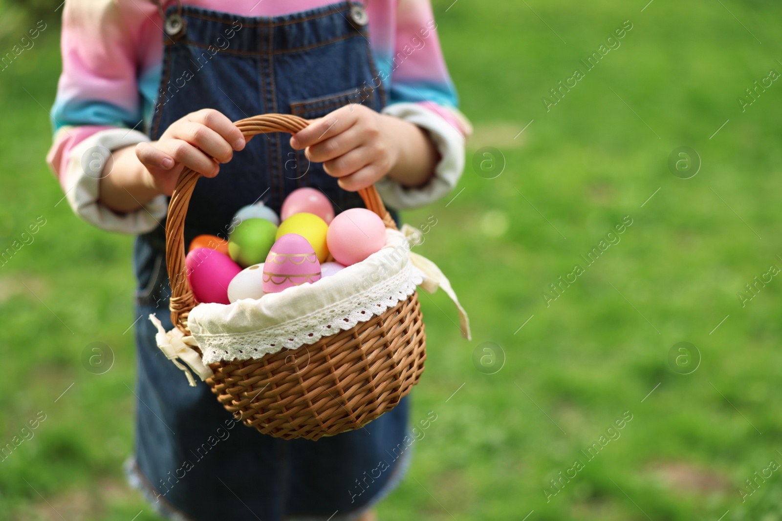 Photo of Easter celebration. Little girl holding basket with painted eggs outdoors, closeup. Space for text