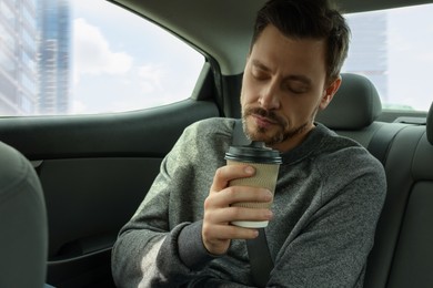 Photo of Sleepy handsome man with cup of coffee in modern car