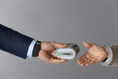 Man giving bribe money to woman on grey background, closeup