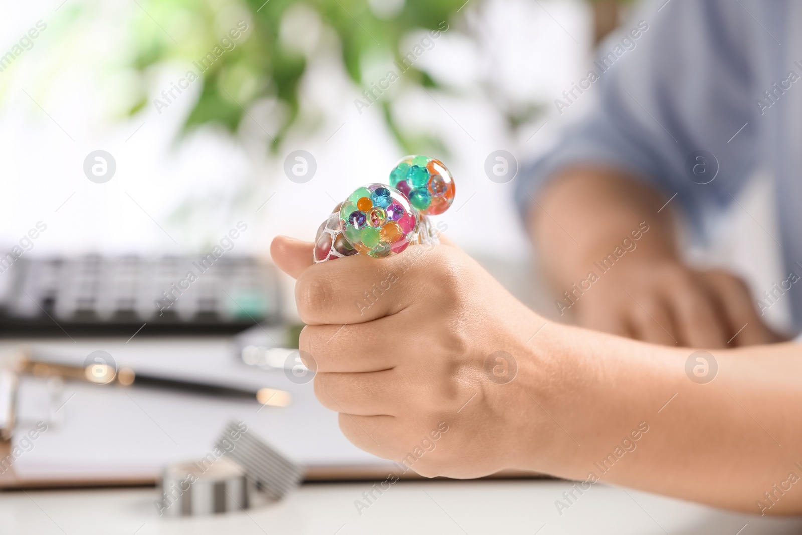 Photo of Woman squeezing colorful slime in office, closeup. Antistress toy