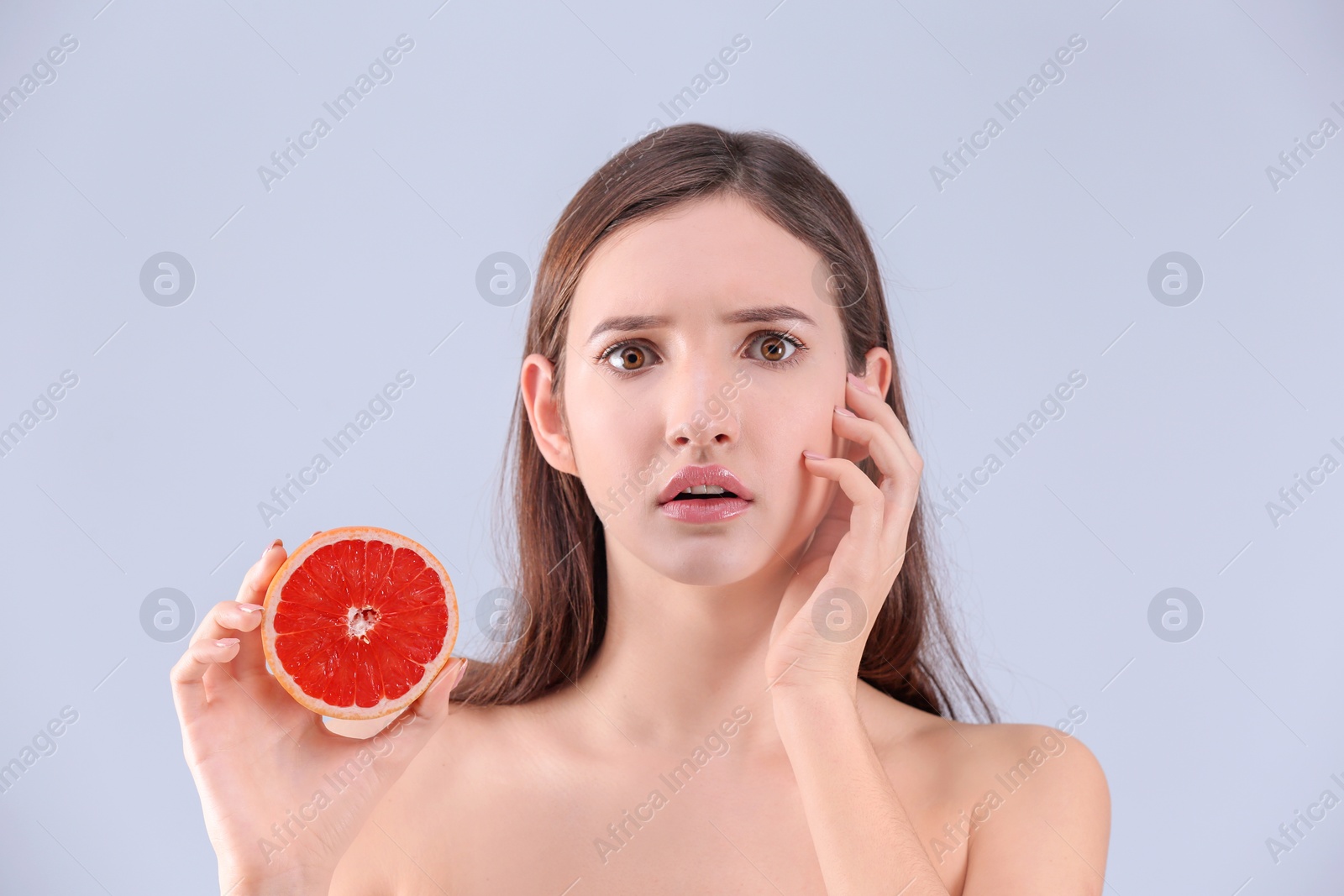 Photo of Teenage girl with acne problem holding grapefruit against grey background