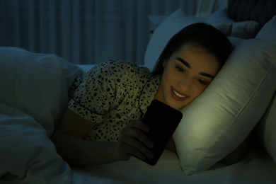 Young woman addicted to smartphone in bed at night