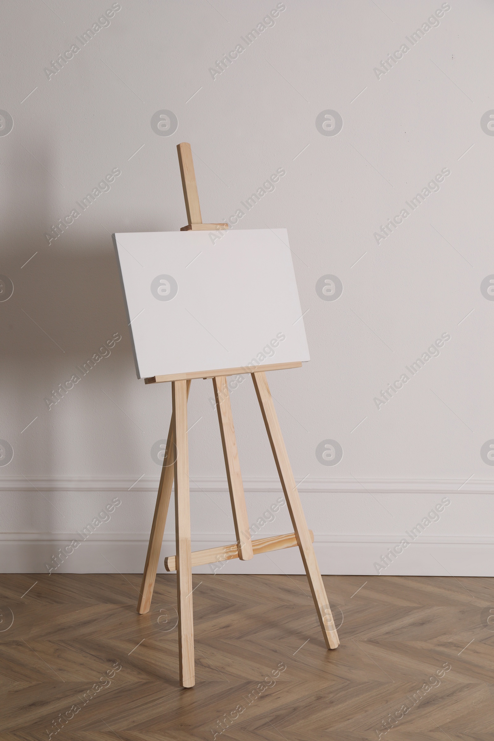 Photo of Wooden easel with blank canvas near light wall