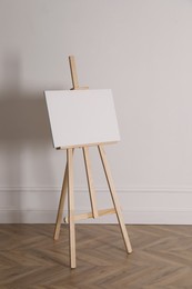 Photo of Wooden easel with blank canvas near light wall