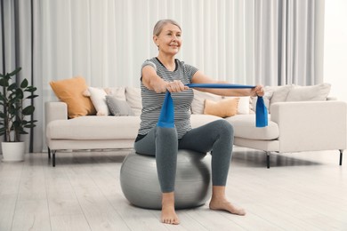 Photo of Senior woman doing exercise with elastic resistance band on fitness ball at home