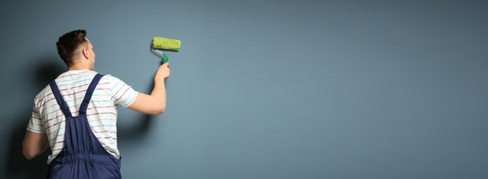 Image of Professional decorator with paint roller near grey wall, space for text. Banner design