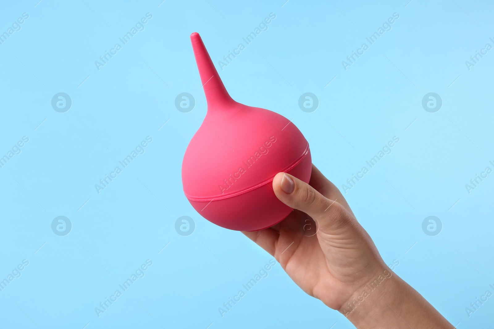 Photo of Woman holding pink enema on light blue background, closeup