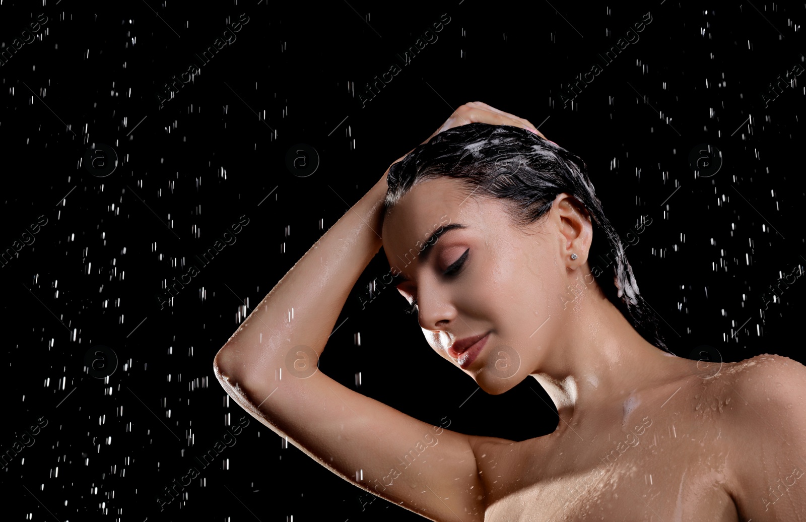 Photo of Young woman washing hair while taking shower on black background