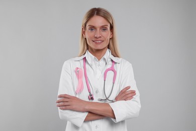 Photo of Doctor with pink ribbon and stethoscope on light grey background. Breast cancer awareness