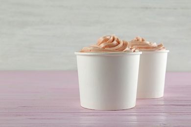 Photo of Cups with tasty frozen yogurt on pink wooden table. Space for text