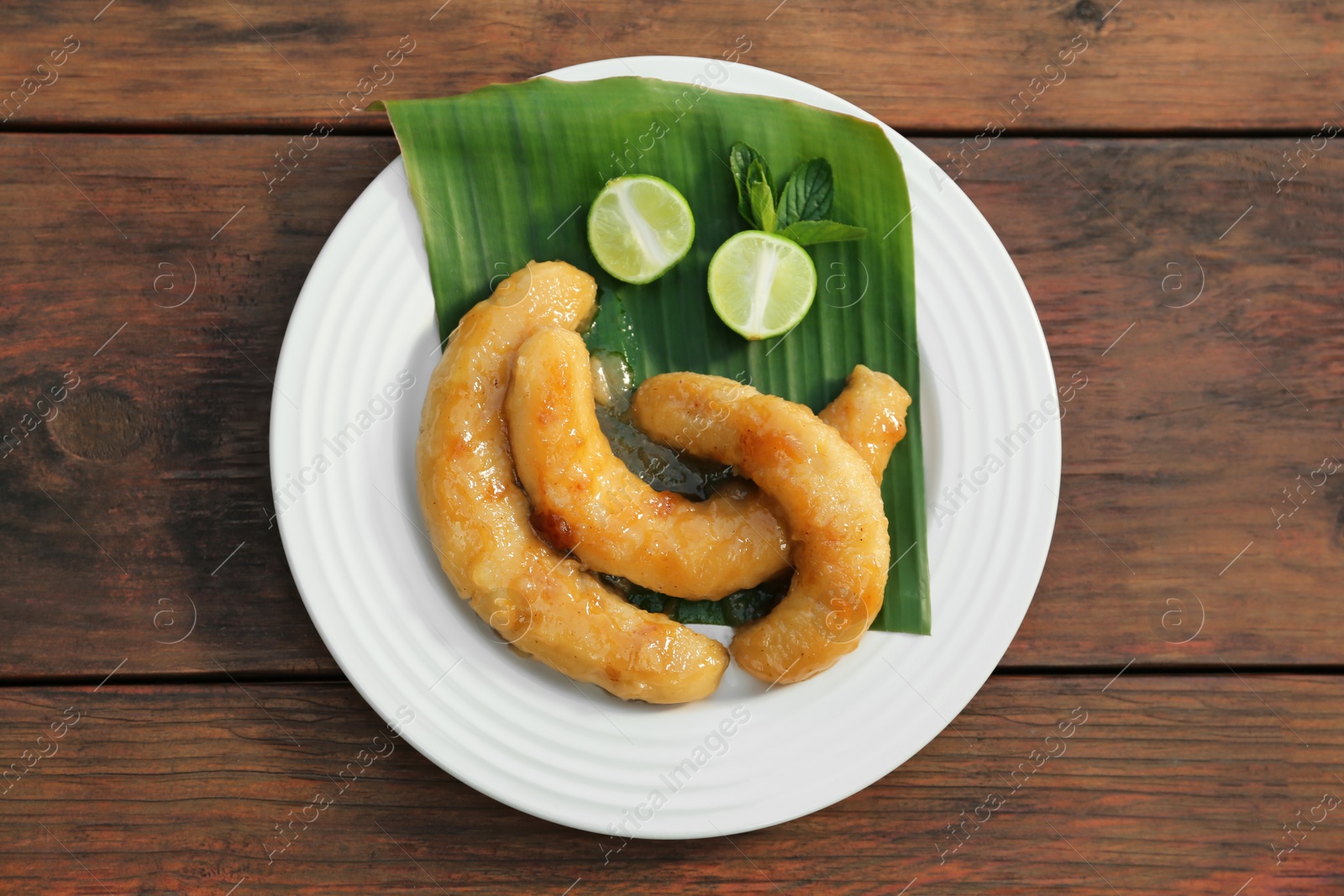 Photo of Plate with delicious fried bananas, lime and mint leaves on wooden table, top view