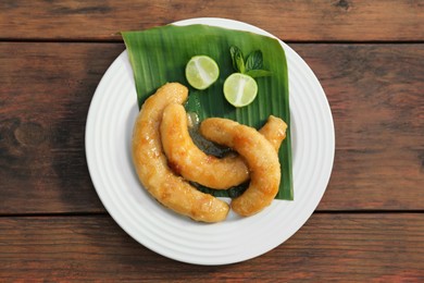 Plate with delicious fried bananas, lime and mint leaves on wooden table, top view