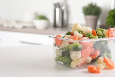 Photo of Mix of different frozen vegetables in plastic container on white textured table in kitchen, space for text