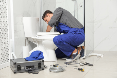 Professional plumber working with toilet bowl in bathroom