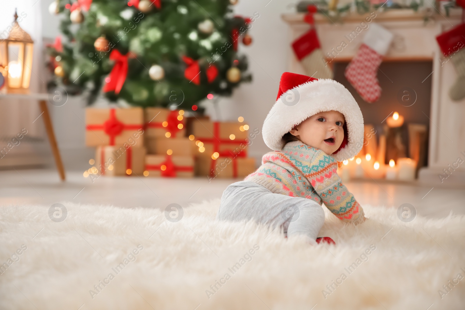 Photo of Cute little baby in Santa hat sitting on fur rug at home. Christmas celebration