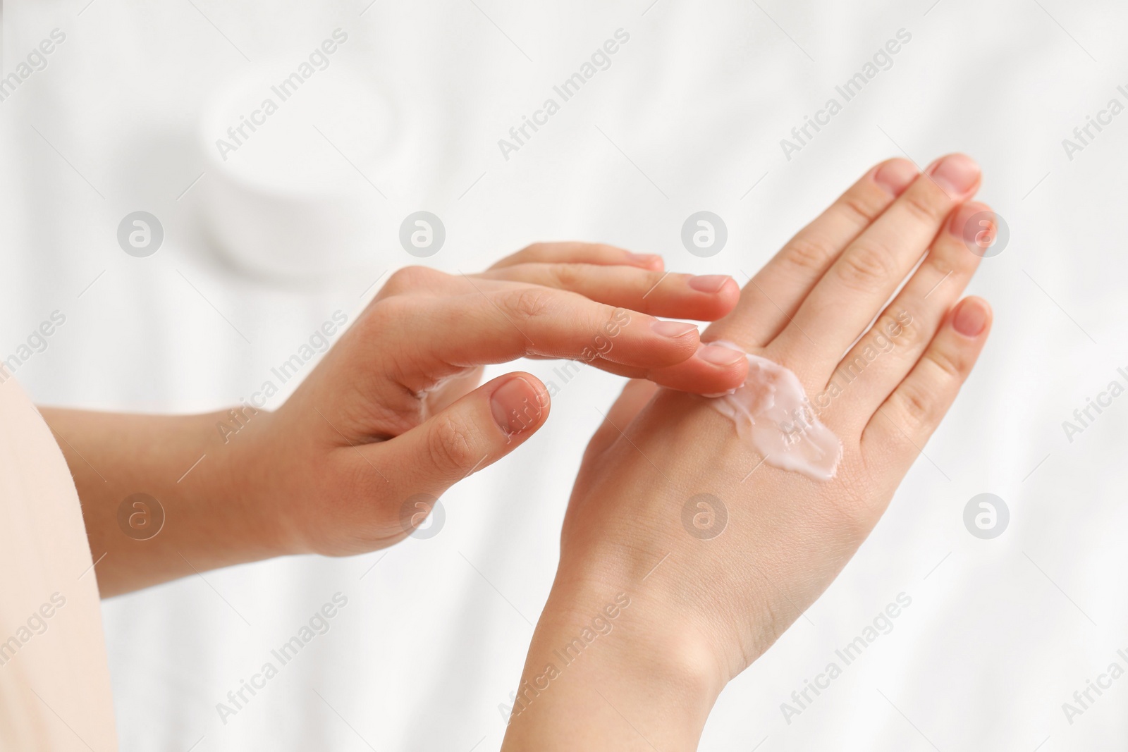 Photo of Young woman with dry skin applying cream onto her hand on bed, closeup