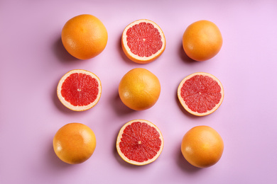 Cut and whole ripe grapefruits on lilac background, flat lay