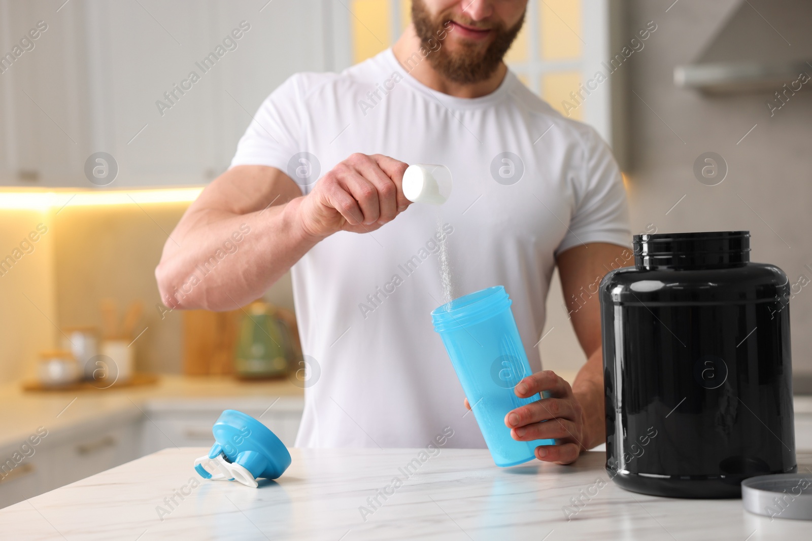 Photo of Young man making protein shake at white marble table in kitchen, closeup