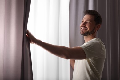 Photo of Happy man opening window curtains at home