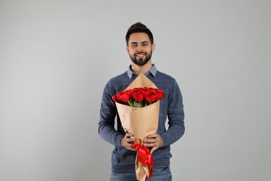 Happy man with red tulip bouquet on light grey background. 8th of March celebration