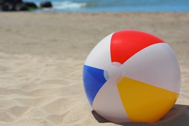 Photo of Colorful beach ball on sand near sea, space for text