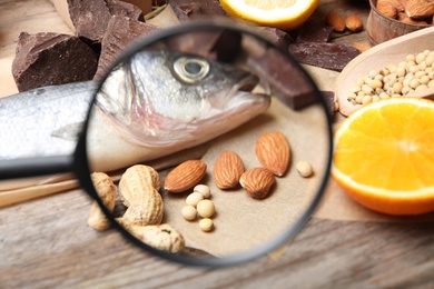 Photo of Different products with magnifier focused on fish and nuts, closeup. Food allergy concept