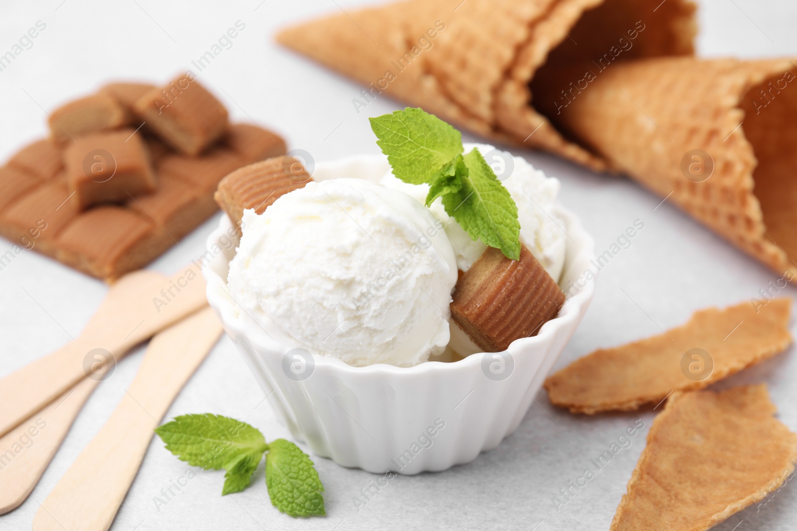 Photo of Scoops of tasty ice cream with mint leaves and caramel candies on white table, closeup