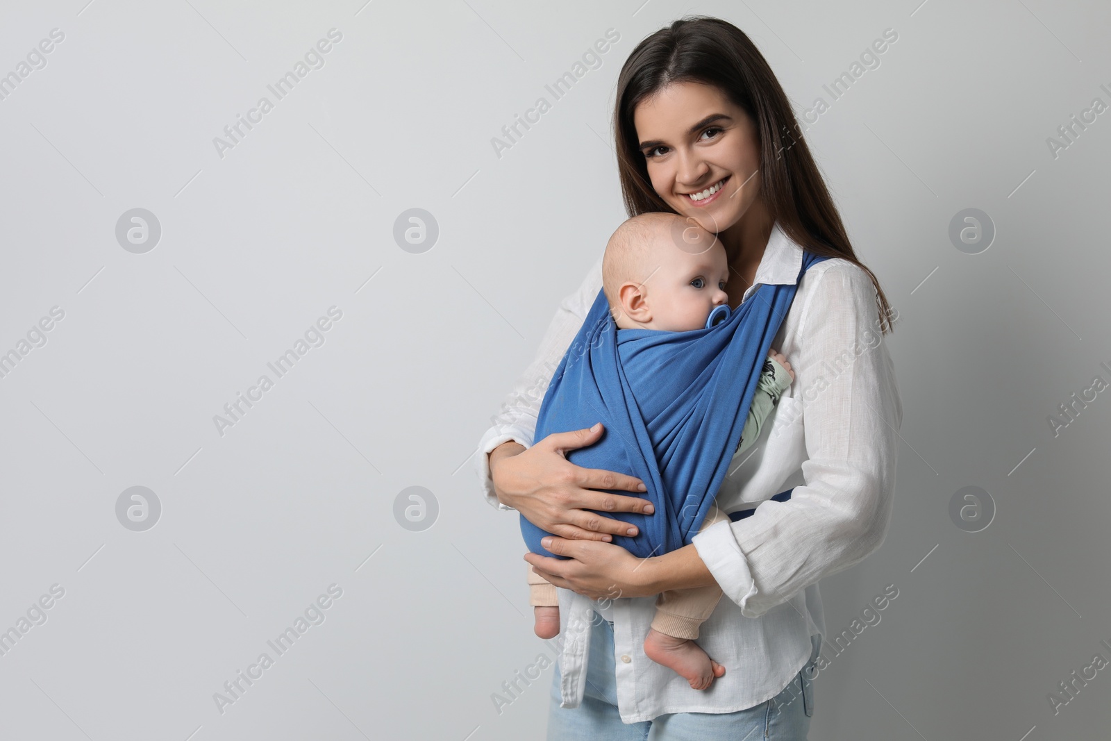 Photo of Mother holding her child in sling (baby carrier) on light grey background. Space for text