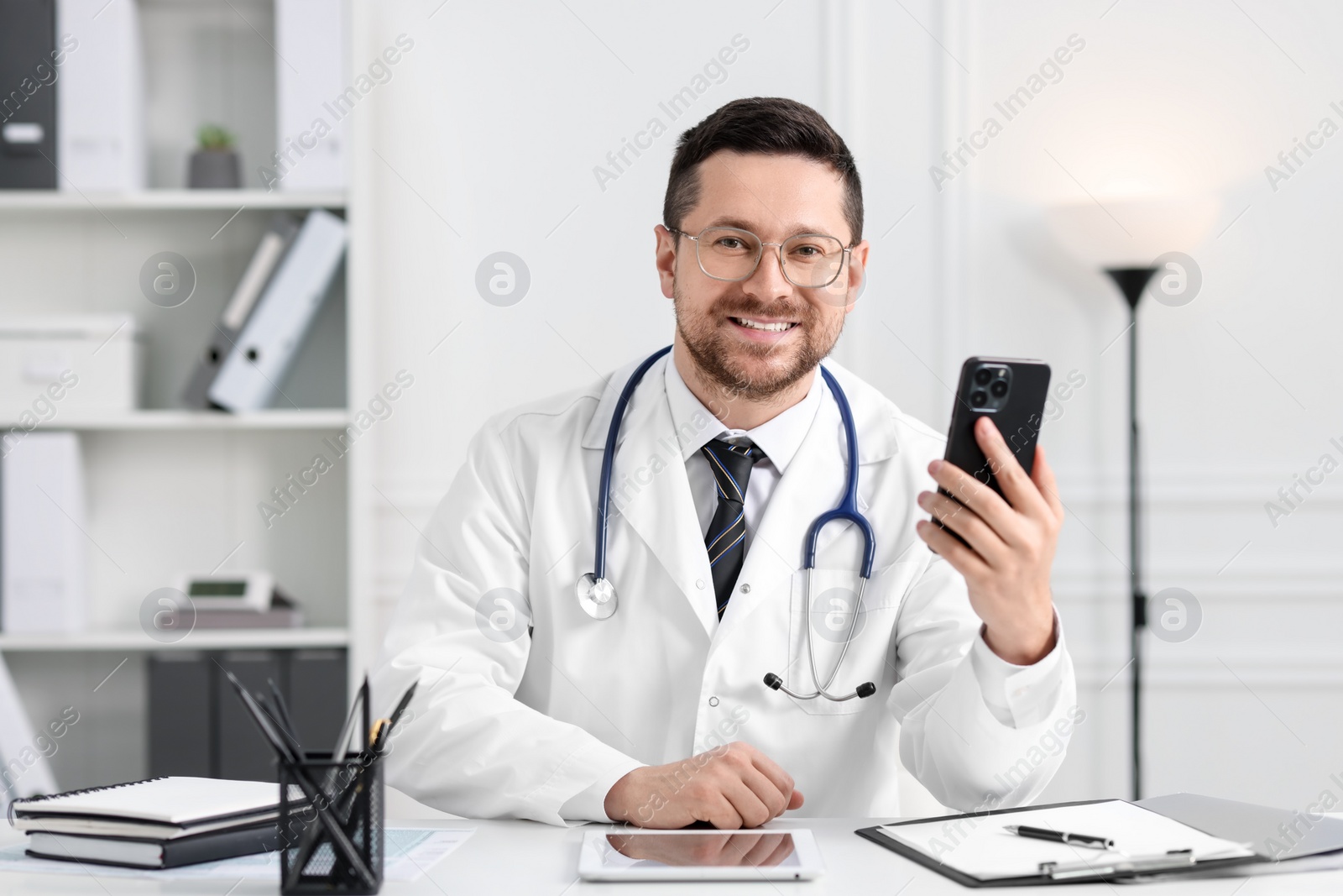 Photo of Doctor with smartphone at table in clinic. Online consultation