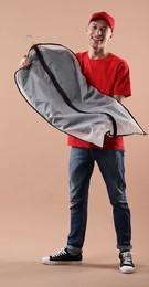 Dry-cleaning delivery. Happy courier holding garment cover with clothes on beige background