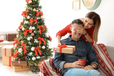 Young woman surprising her boyfriend with Christmas gift at home