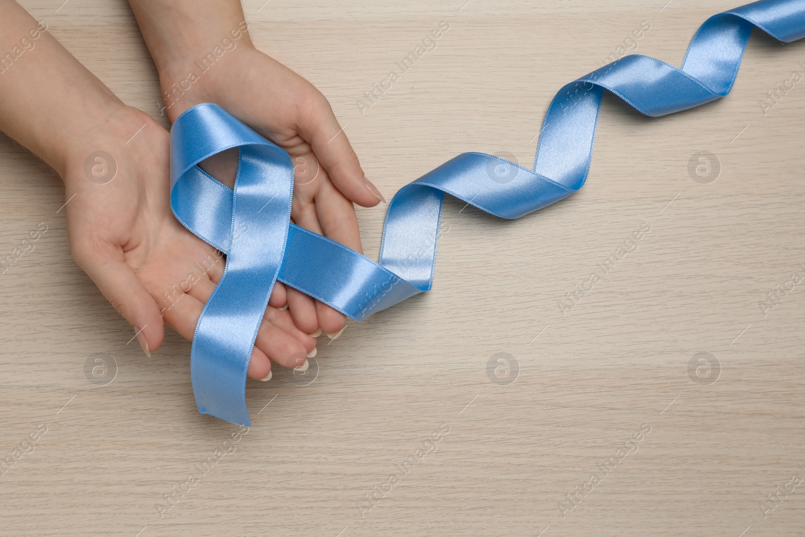 Photo of Woman holding light blue awareness ribbon at wooden table, top view. Space for text