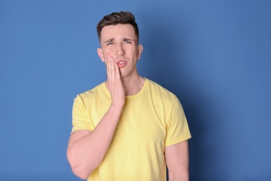 Young man with sensitive teeth on color background