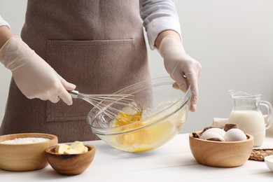 Photo of Woman whisking crepe batter in glass bowl at white wooden table, closeup