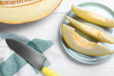 Photo of Sliced delicious ripe melon and knife on white wooden table, flat lay