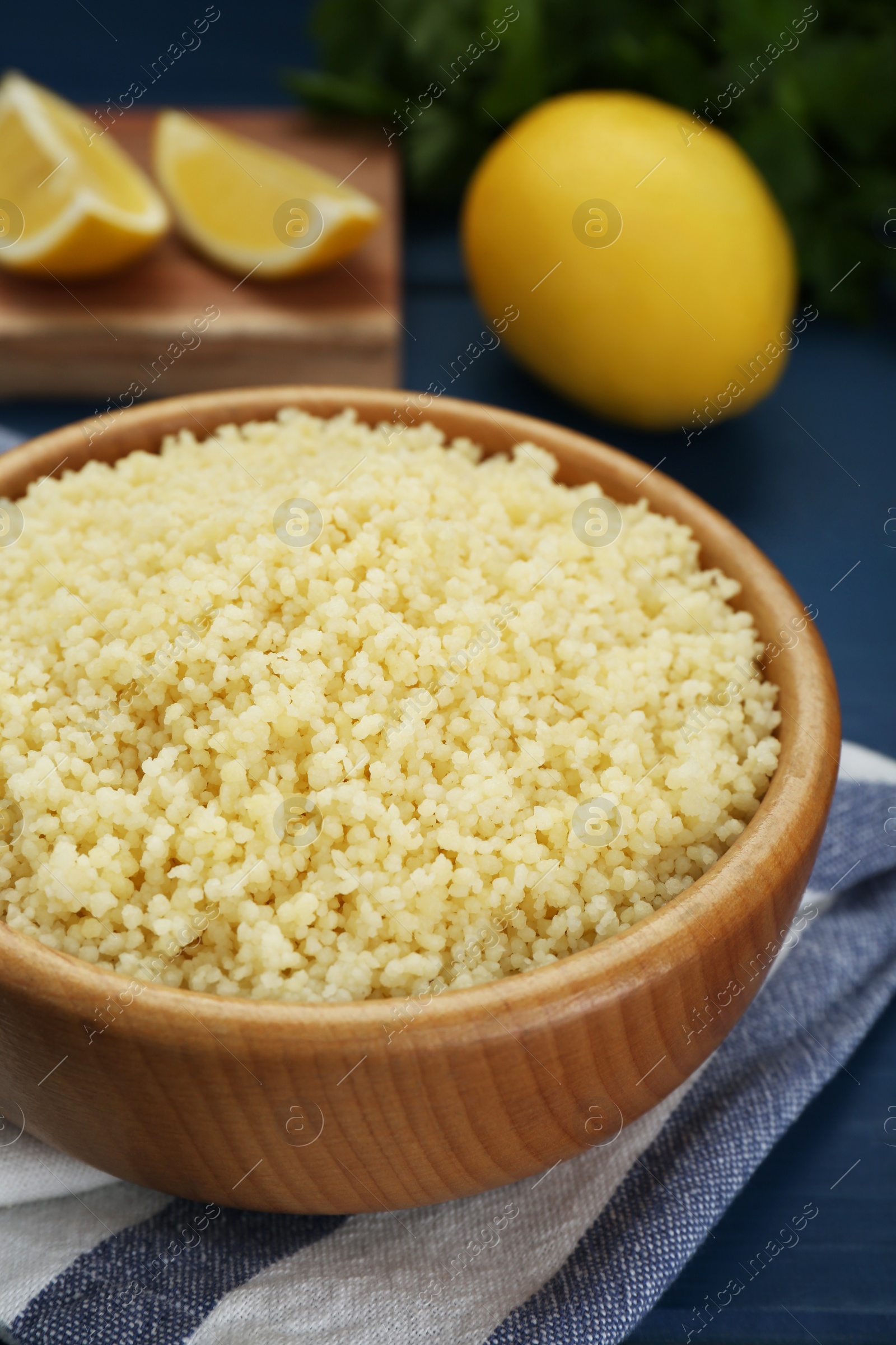 Photo of Bowl of tasty couscous on blue wooden table, closeup