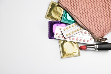 Photo of Flat lay composition with birth control pills and condoms on light background, space for text. Safe sex concept